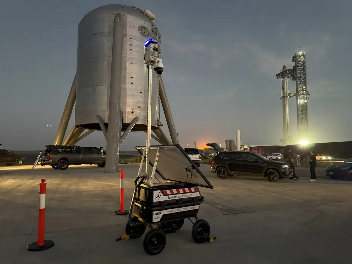 A LOBO tower at dusk with its light on, beside a test vehicle and a lit launch tower.