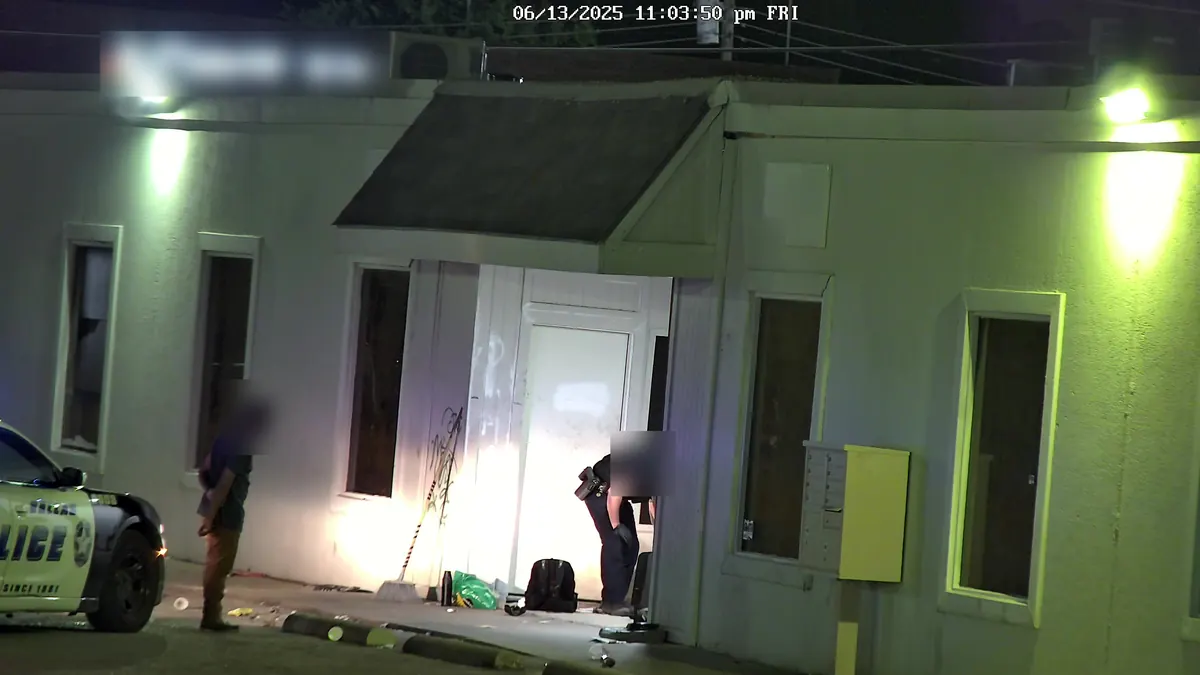 Tower camera at night: a police car and an officer at a building's door, with a man standing by.