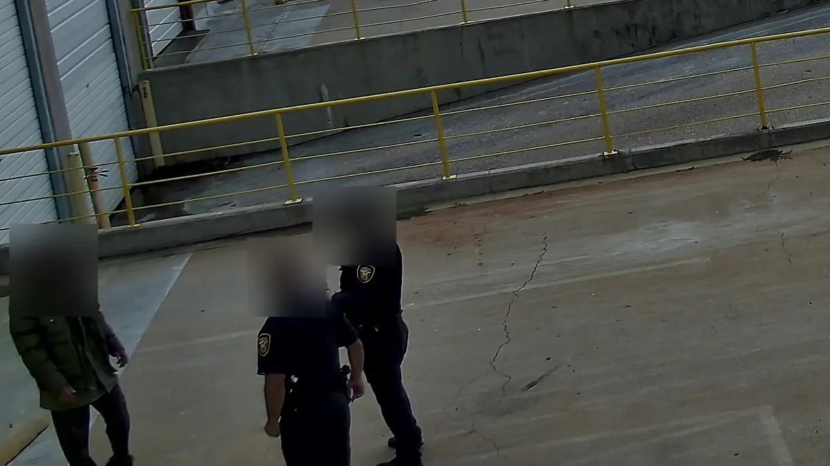 Tower camera in daylight: two police officers with a man at a loading dock.