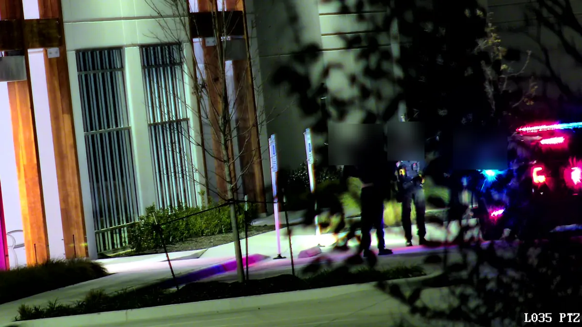 Tower camera at night: a police car with its lights on and officers with a person beside a new building.