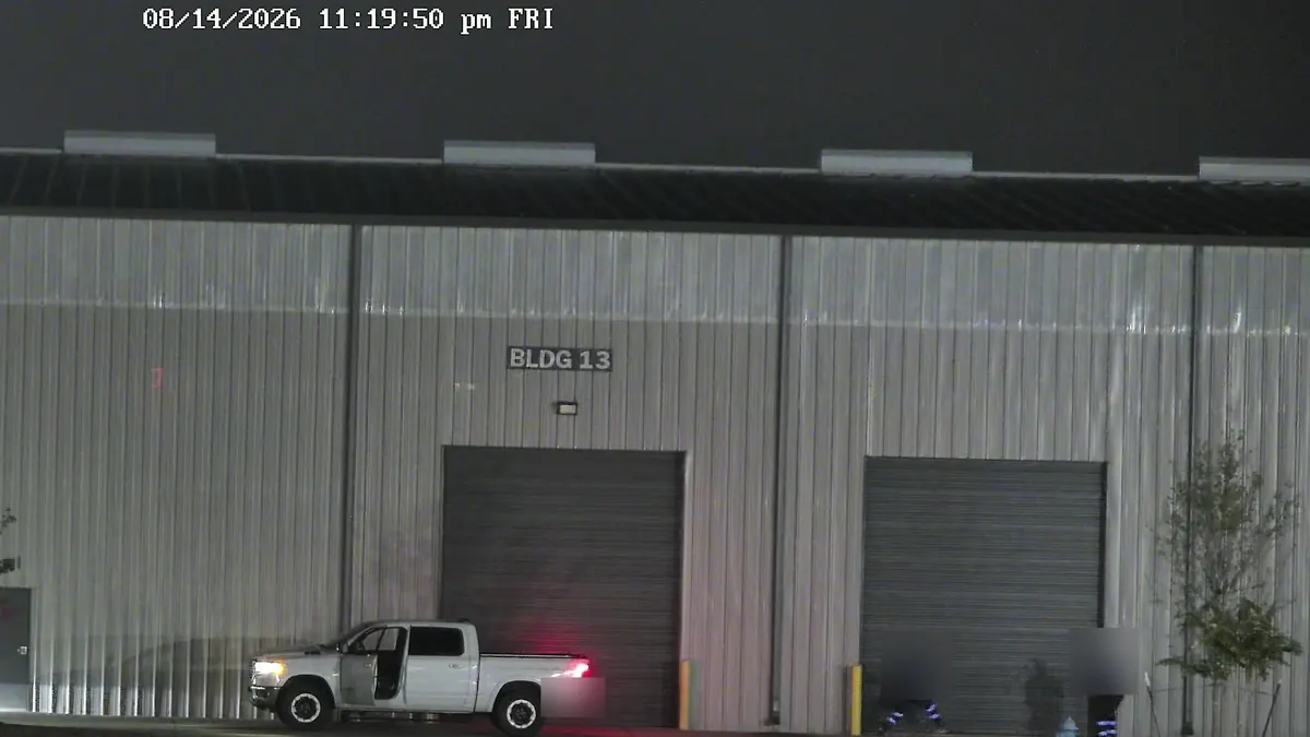 Tower camera at night: a pickup at a warehouse's dock doors, with two people at the next door.